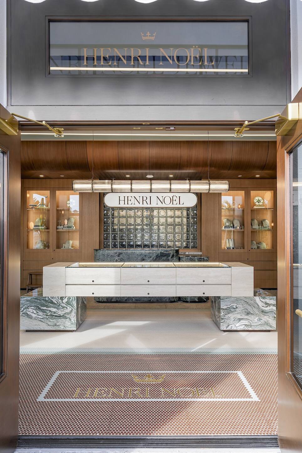 Henri Noël jewelry store entrance with glass doors, marble counters, wall display shelves, and the Henri Noël logo featured above and on the floor mat.