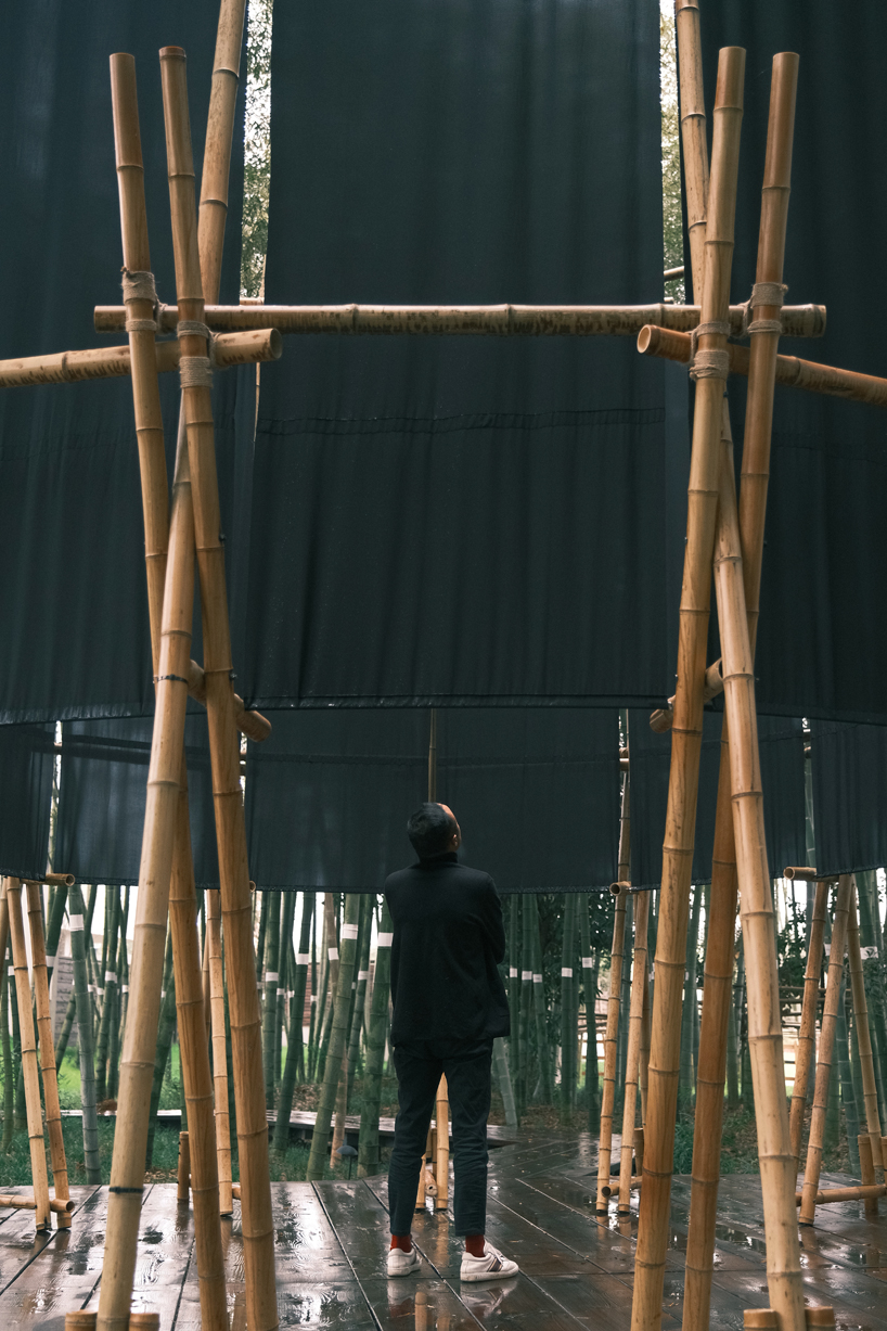 A black fabric veil hovers within a raw bamboo matrix in hubei’s dense grove