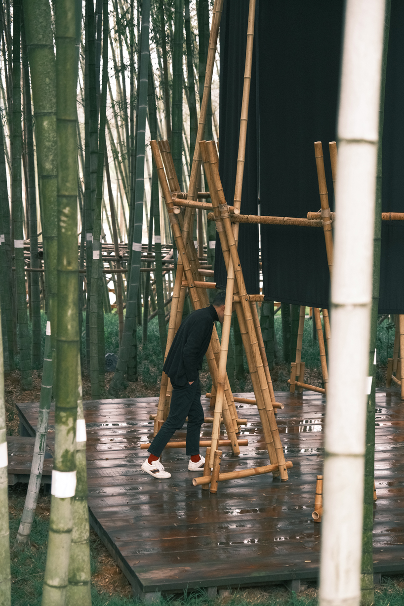 A black fabric veil hovers within a raw bamboo matrix in hubei’s dense grove