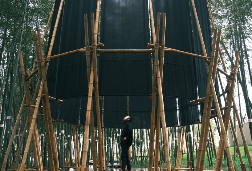 A black fabric veil hovers within a raw bamboo matrix in hubei’s dense grove