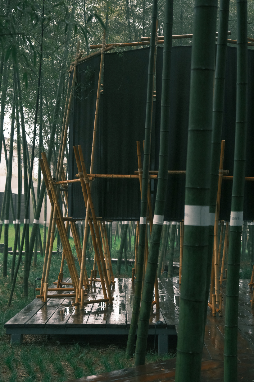 A black fabric veil hovers within a raw bamboo matrix in hubei’s dense grove