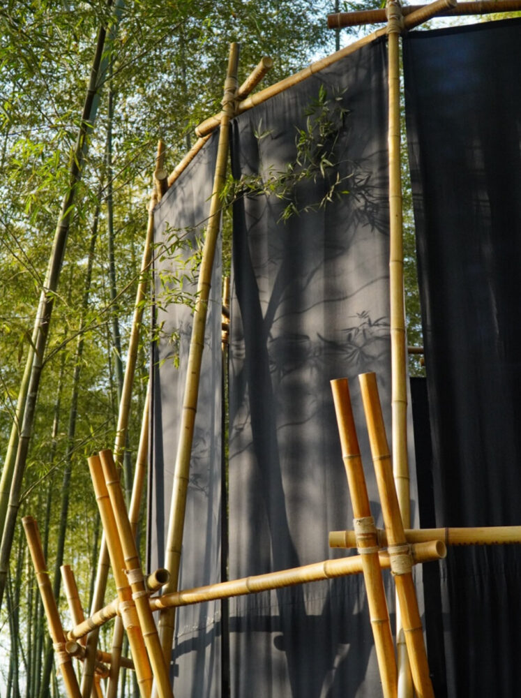 A black fabric veil hovers within a raw bamboo matrix in hubei’s dense grove
