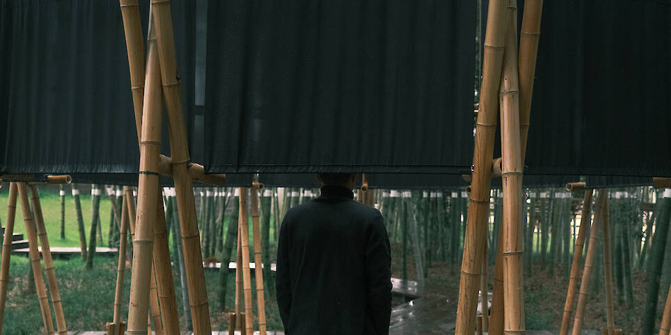 A black fabric veil hovers within a raw bamboo matrix in hubei’s dense grove
