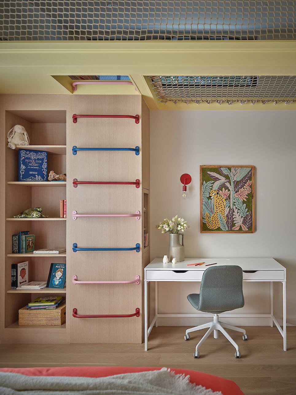 Children’s bedroom in a Gillian Gillies Net Zero Ready Home, featuring a climbing ladder, built-in shelves with books and toys, a white desk with a chair, flowers, and a frame