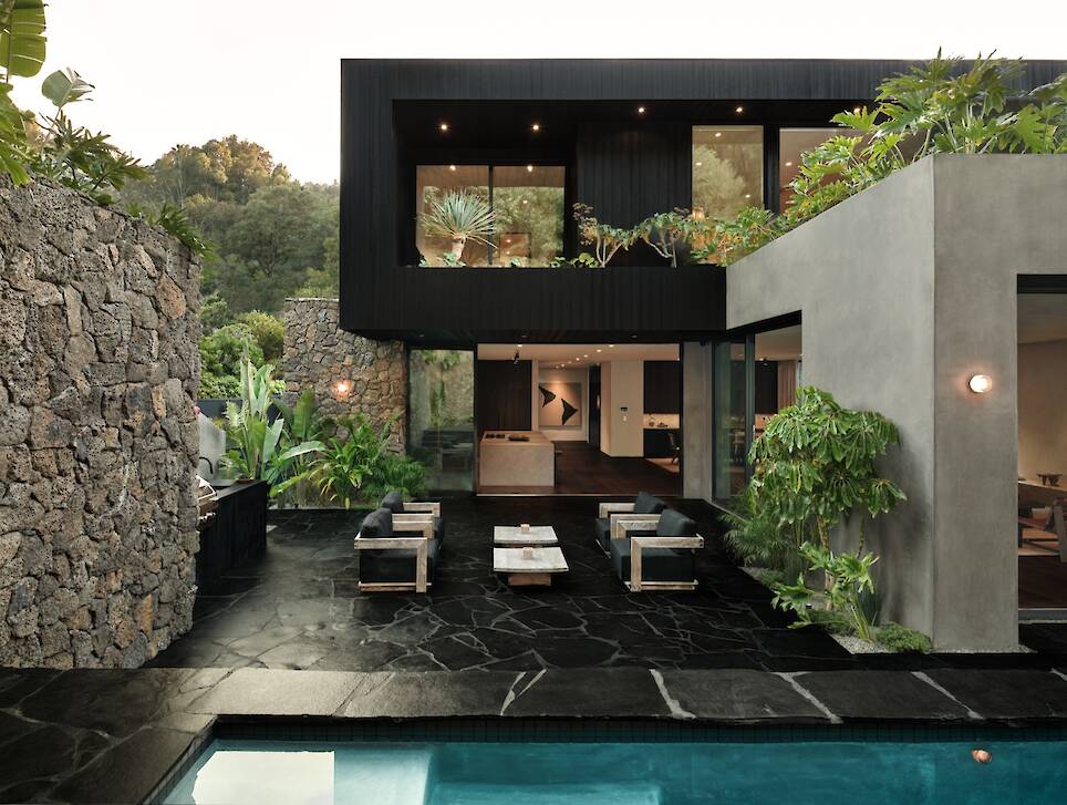Obsidian House: A modern house with large windows, outdoor seating area, striking stone walls, lush plants, and a swimming pool in the foreground
