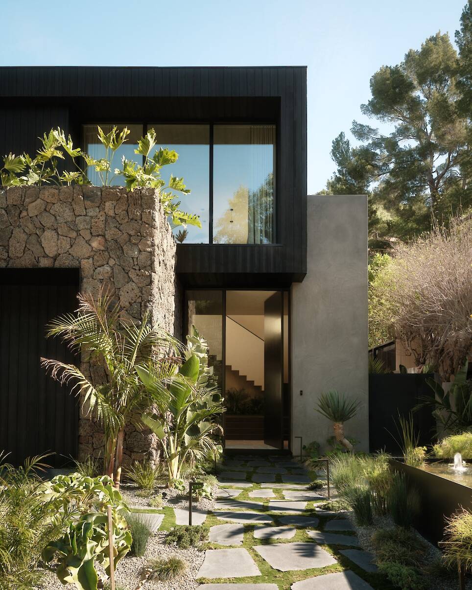 Modern two-story Obsidian House with stone and dark wood exterior, large windows, and a landscaped walkway surrounded by greenery and a small pond