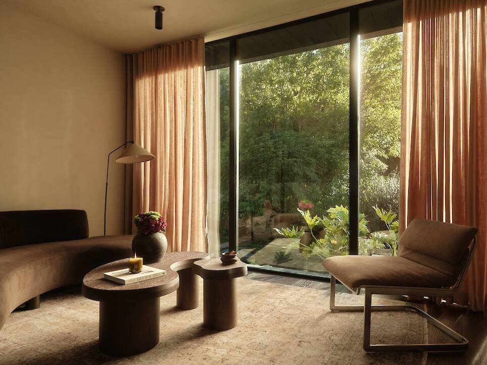 A modern living room at Obsidian House with warm, neutral tones, a curved brown sofa, a wooden coffee table, a sleek chair, and large floor-to-ceiling windows looking out onto a