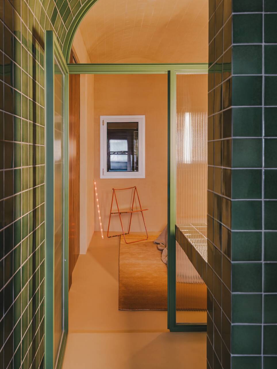 A green-tiled doorway leads to a room with orange walls, a window, a tan rug, a pink ladder, and a cushion on the floor. Vertical light strip glows by the wall