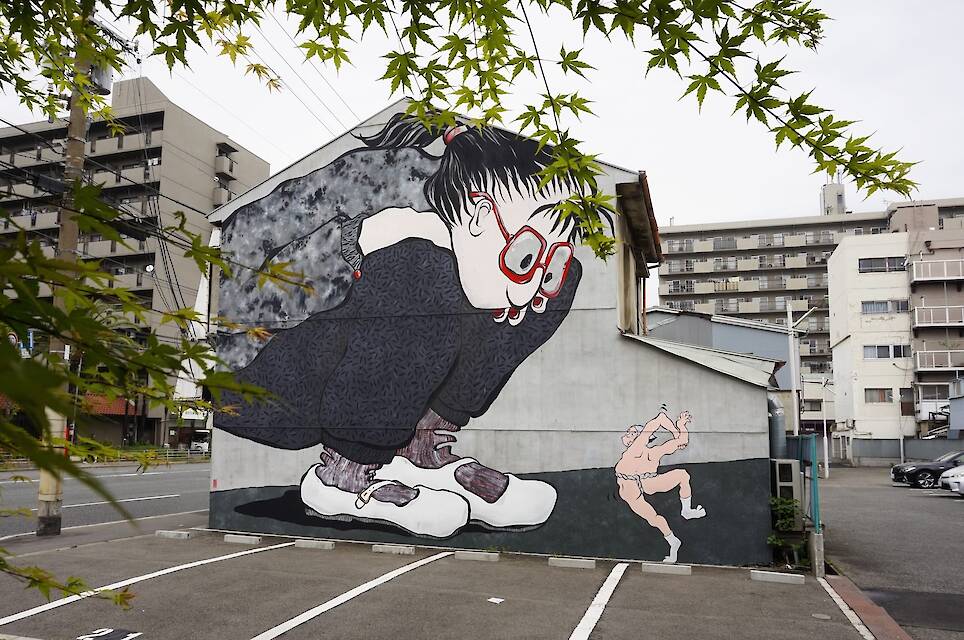 a mural by Ella & Pitr on a wall featuring two cartoonish figures, very large and looking down at a very small dancing figure without clothes on