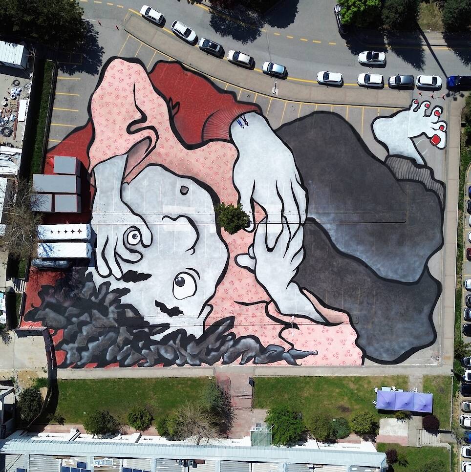an aerial view of a large mural by Ella & Pitr on the ground of a public square featuring two cartoonish figures in an embrace