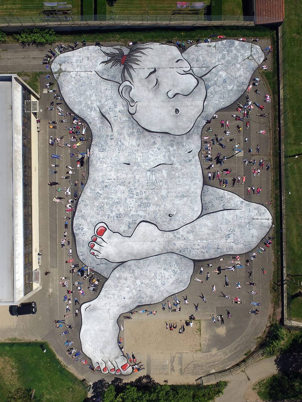 an aerial view of a large mural by Ella & Pitr on the ground of a public square featuring a cartoonish sleeping figure