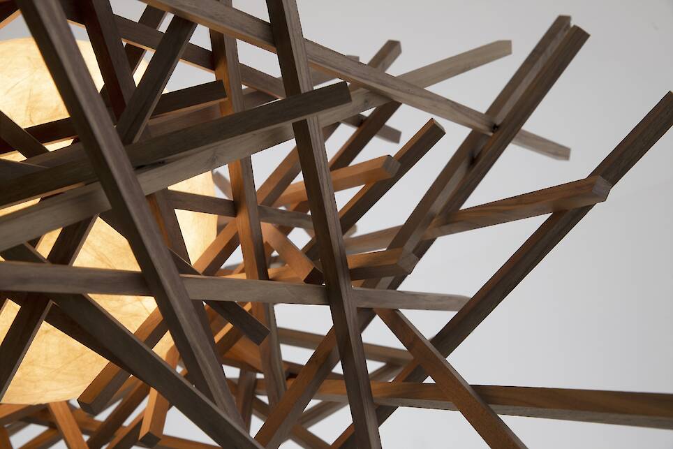 A close-up of a geometric wooden light fixture, designed by Nick Sheridan for Cerno, with interlocking wooden rods surrounding a glowing spherical light source