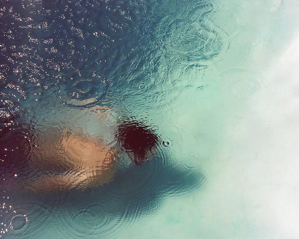 Person swimming underwater with ripples and raindrops visible on the surface of the water