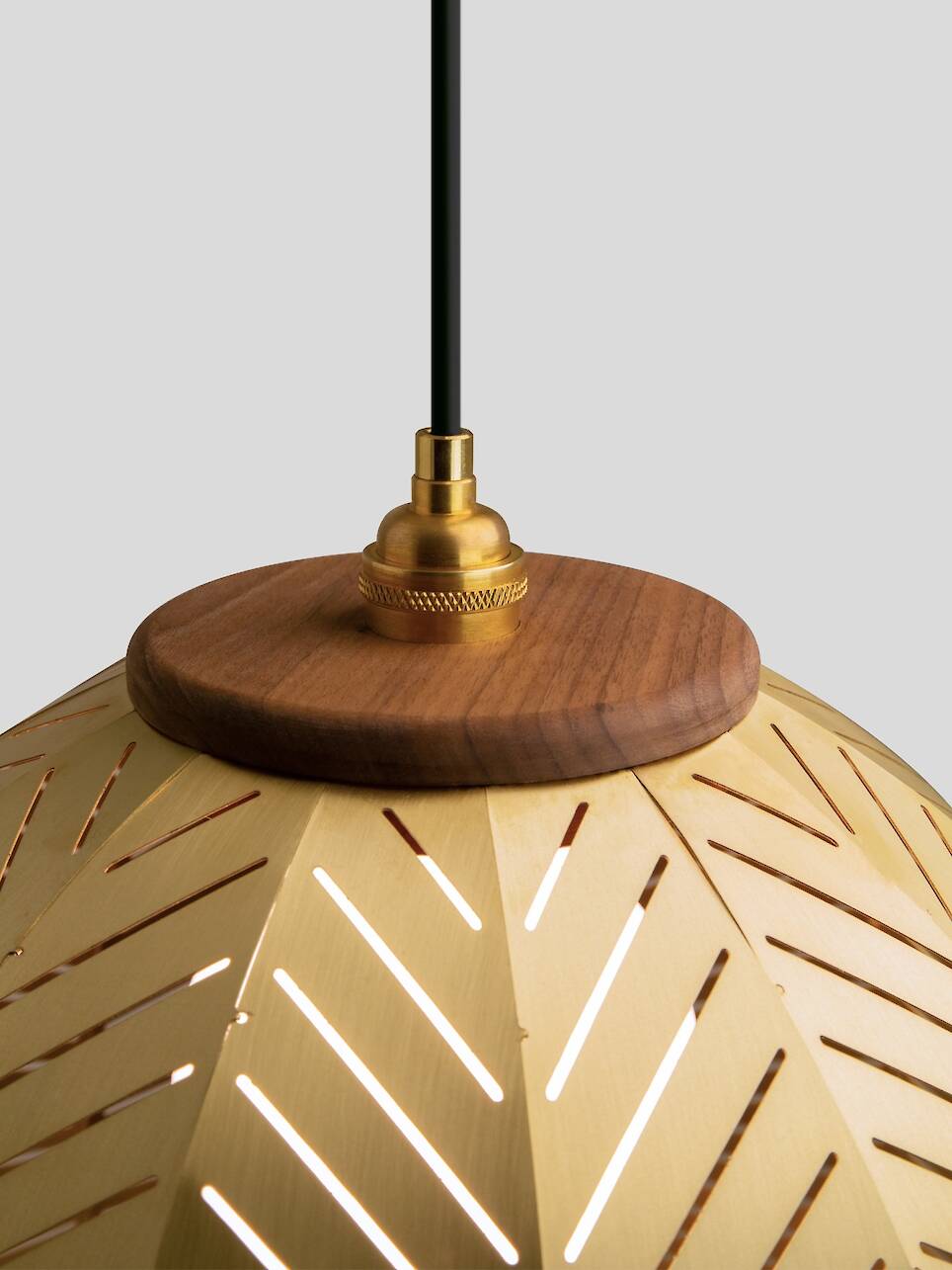 Close-up of a hanging pendant light, designed by Nick Sheridan for Cerno, with a gold metal shade featuring diagonal cutouts, topped with a wooden accent and brass fixture again