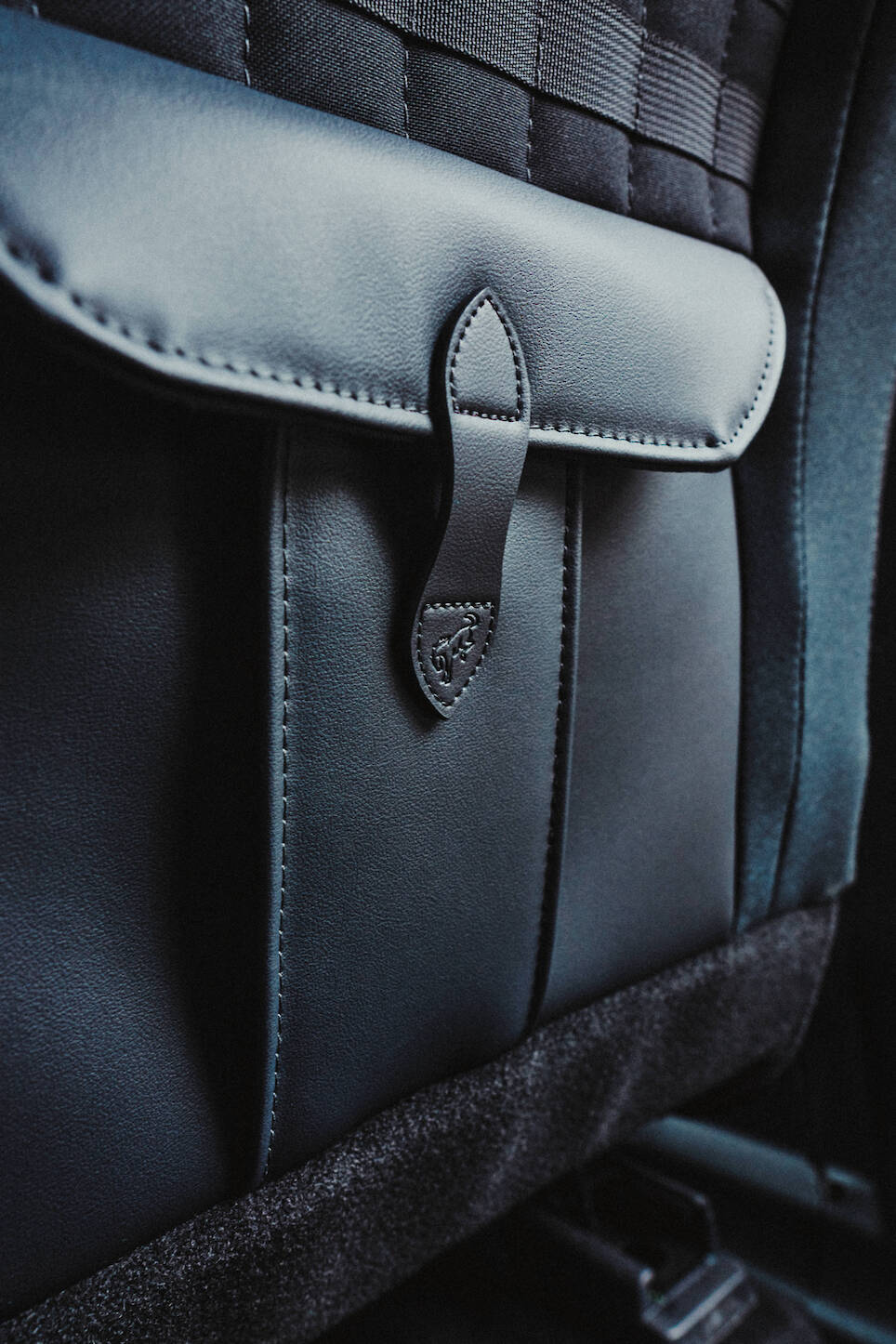 Close-up of a black leather seat-back pocket with a stitched flap and tab closure in a car interior