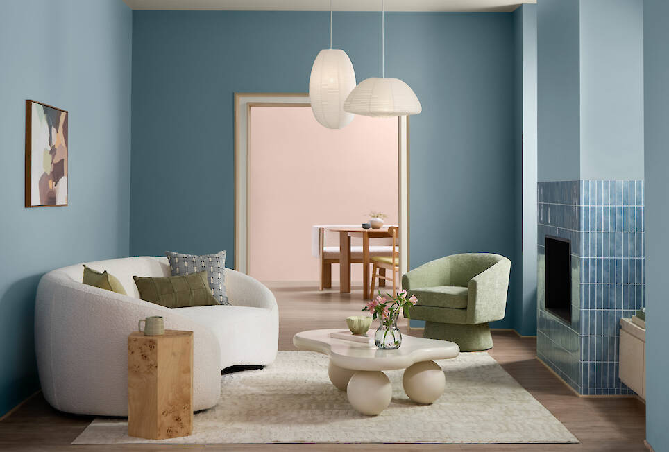 Modern living room with Valspar 2027 Color of the Year blue walls, a white curved sofa, green chair, abstract art, two pendant lights, and a round table with flowers; a dining a