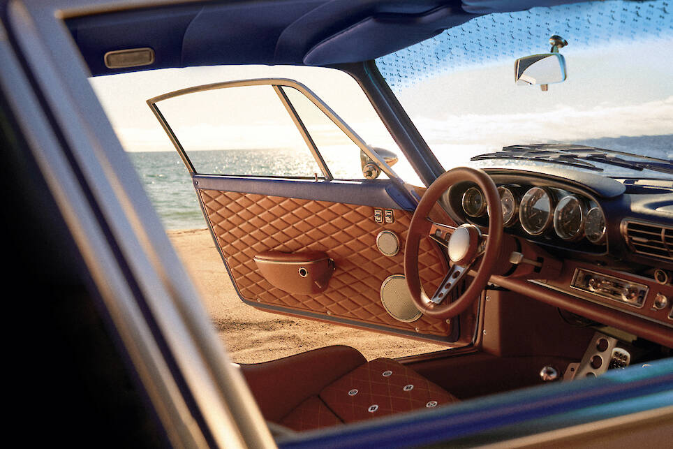 Open door of a Singer Louis Vuitton Porsche 911 with brown quilted leather interior, parked by the sea, sunlight reflecting on the water