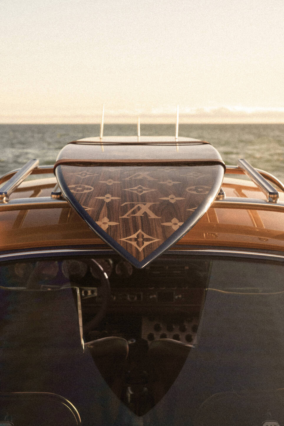 A surfboard with a designer pattern is mounted on the roof of a classic Singer Louis Vuitton Porsche 911, parked by the ocean at sunset