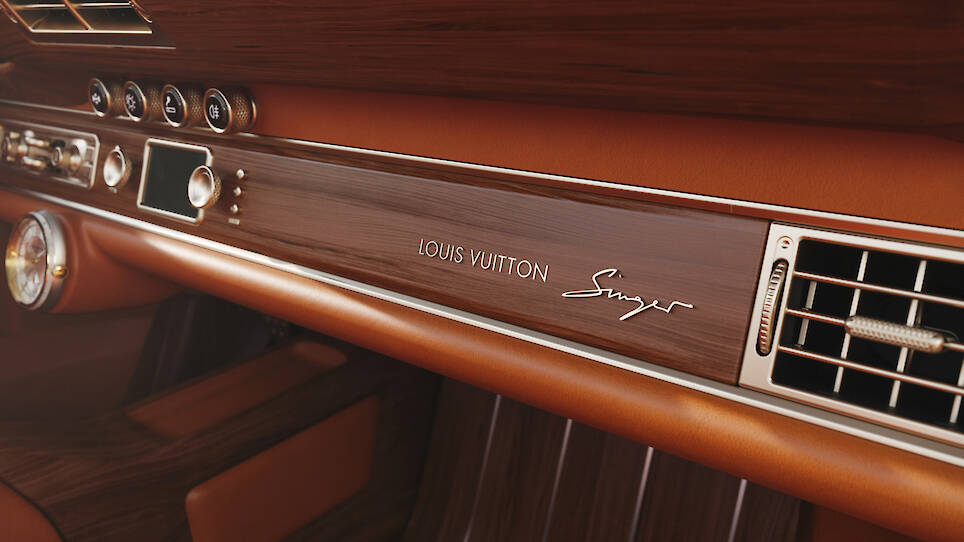 Close-up of a car dashboard featuring elegant wood paneling, air vents, leather trim, and the Singer Louis Vuitton Porsche 911 logos finely engraved on the panel