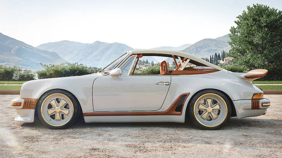 Side view of a vintage-style white Singer Louis Vuitton Porsche 911 with tan accents, parked outdoors on a sunny day with mountains and greenery in the background