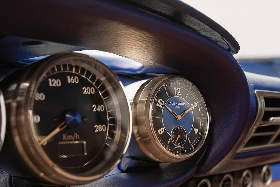 Close-up of a car dashboard showing a speedometer in km/h and a blue Louis Vuitton-branded analog clock, set inside the luxurious cabin of a Singer Louis Vuitton Porsche 911
