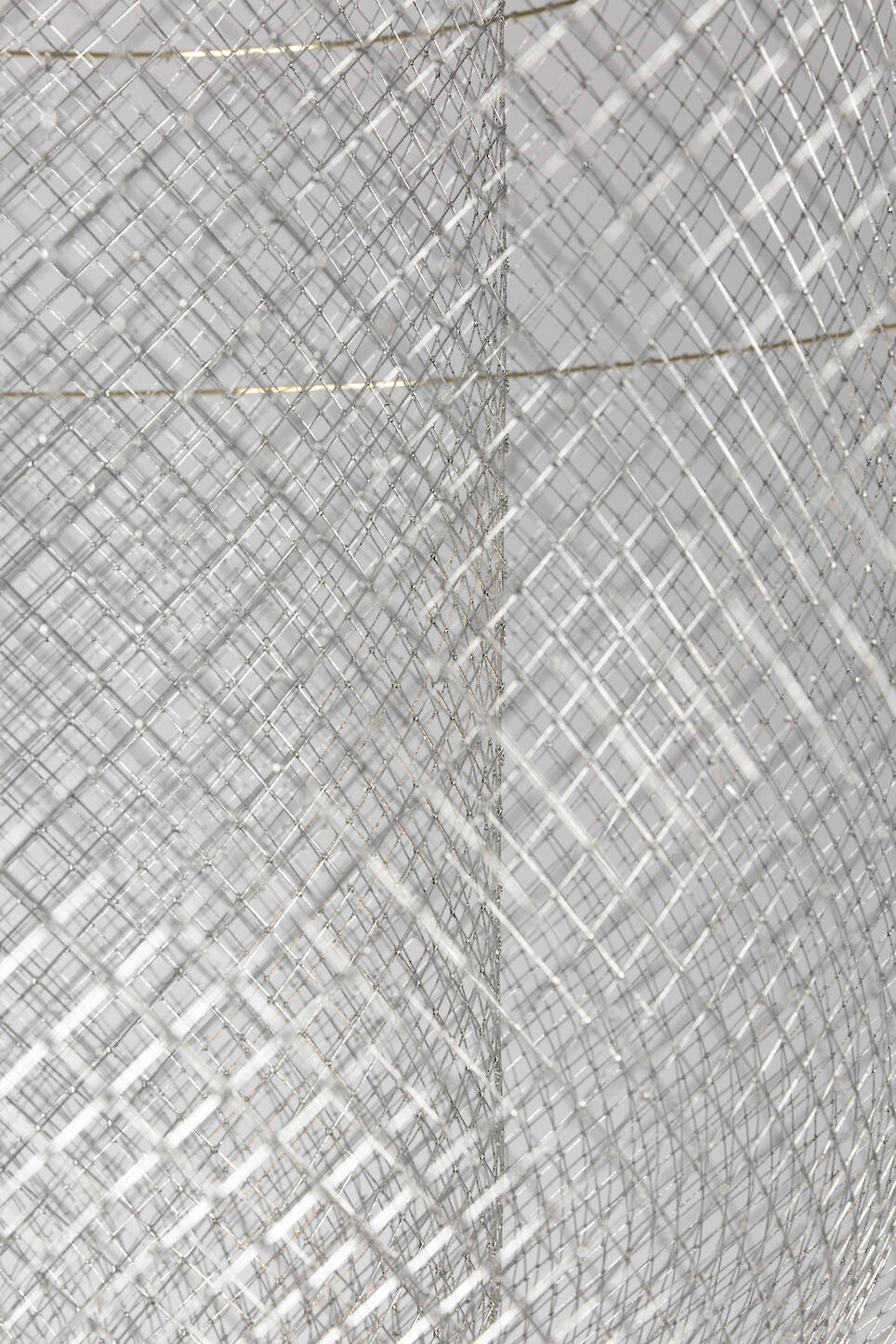 Close-up of overlapping metallic wire mesh panels, reminiscent of Rick Tegelaar’s innovative designs, creating a geometric, grid-like pattern with intersecting lines on a neut