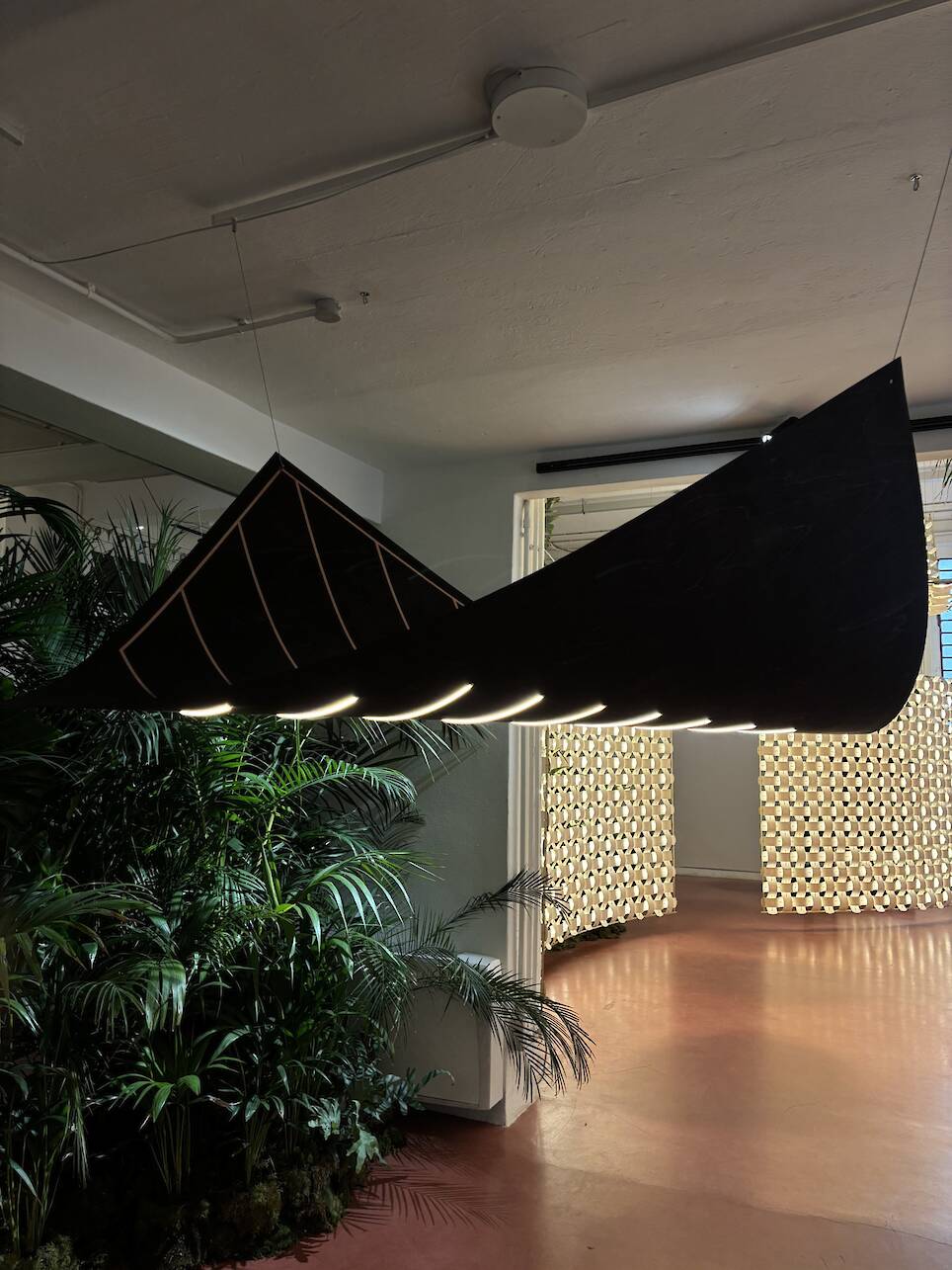A black canoe is suspended from the ceiling, with lights installed inside it—a striking installation reminiscent of Rick Tegelaar’s innovative approach to lighting design. G