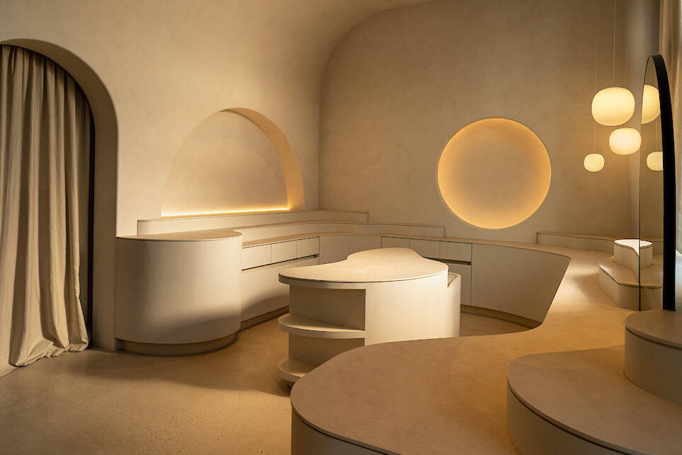 Minimalist interior with curved cream-colored furniture, round wall insets, and soft, warm lighting from circular pendant lights and recessed fixtures against smooth, beige wall