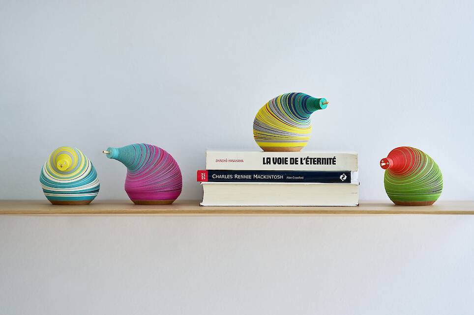 a series of small paper figures made from numerous layers of colored paper on a flexible central axis so that they look like anthropomorphized pears