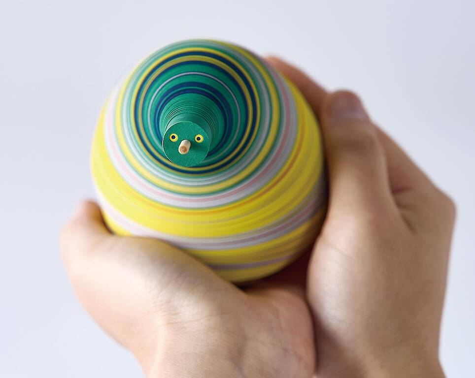 a small paper figure made from numerous layers of colored paper on a flexible central axis so that it looks like an anthropomorphized pear