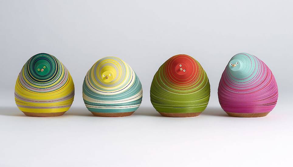 a series of small paper figures made from numerous layers of colored paper on a flexible central axis so that they look like anthropomorphized pears