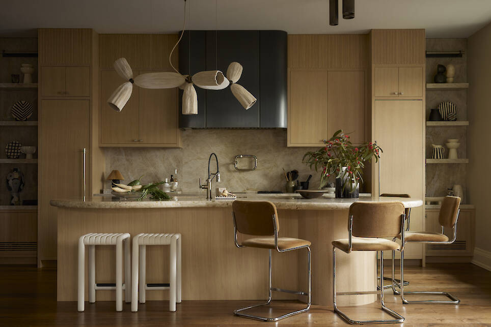 Modern kitchen with light wood cabinets, marble backsplash, and an island with tan chairs. A sculptural pendant light hangs above the island, elevating the space in this stunnin