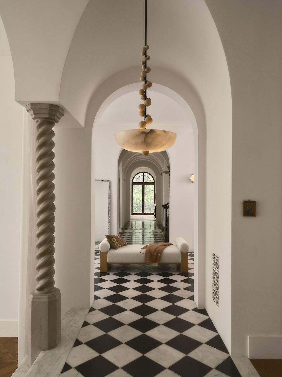 Arched hallway with a checkered black-and-white floor, a modern chandelier, and a minimalist daybed from the Venus Williams Crate & Barrel collection at the end near a large win