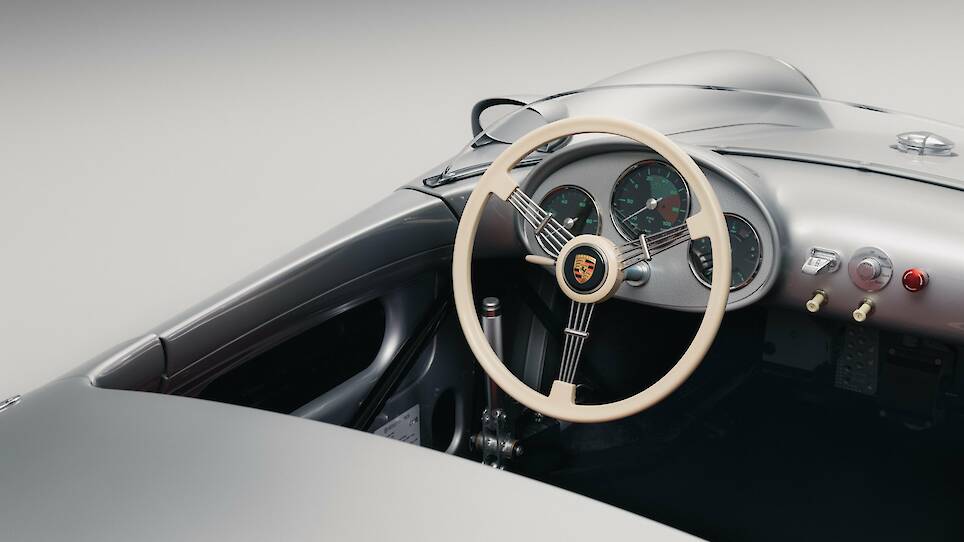Close-up of a classic silver Porsche 550 J car interior showing the beige steering wheel, dashboard, and instrument panel with Porsche emblem