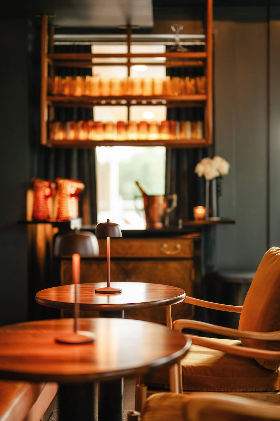 Cozy lounge at Dexter Hotel Michigan with wooden tables, modern table lamps, orange cushioned chairs, bar shelves with glassware, and soft ambient lighting