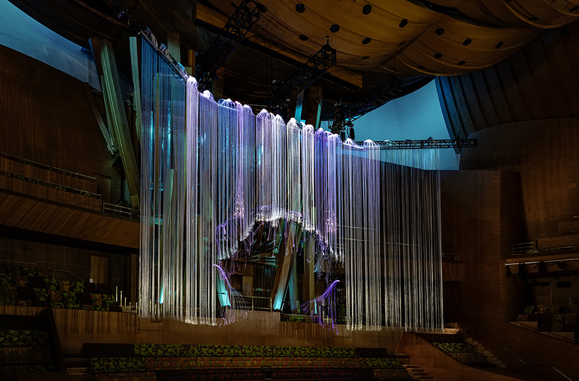 the installation in a blue and violet state, showing the full width of the work against the hall’s timber interior