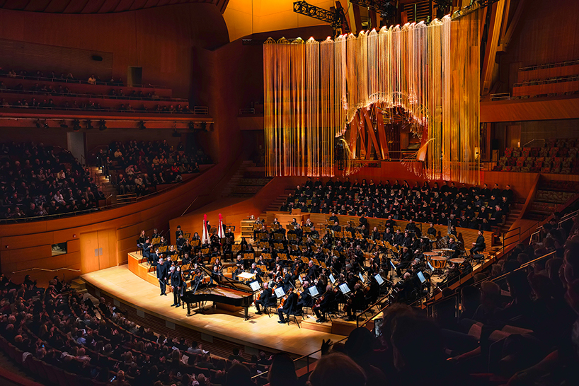 the sequence shifts to amber, carrying the color across the suspended strands, the stage, and the seating