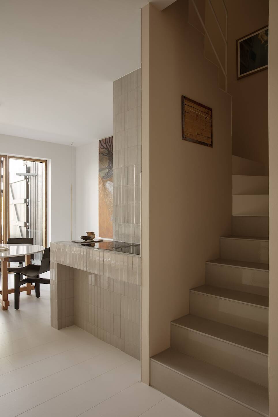 Modern interior with beige tiled staircase and matching breakfast bar, wooden dining table with chairs in background, and minimalist decor in neutral tones