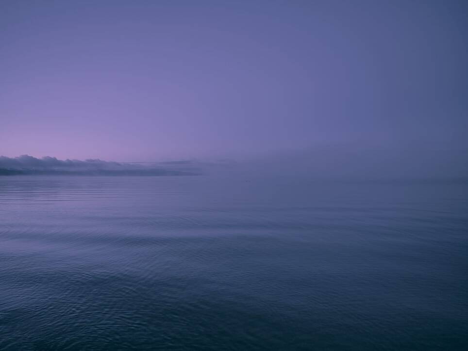 an open body of water with a slice of land in the distance, hued purple at sunrise