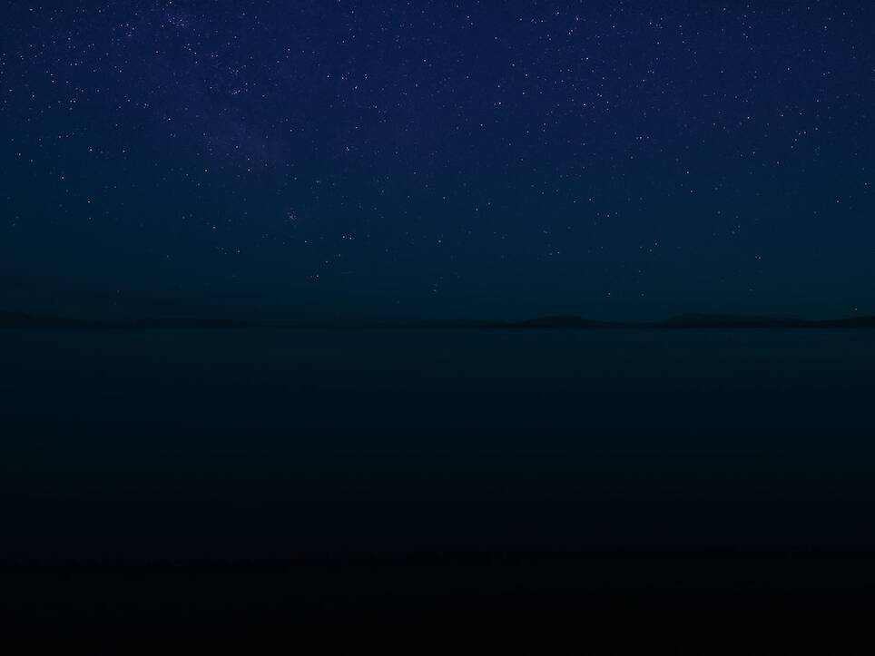 a nighttime scene on an open body of water with stars in the sky