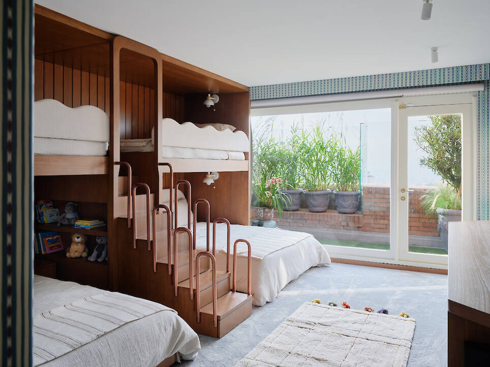 A wooden bunk bed unit with a built-in staircase and lower full-size bed, situated in a bedroom with a sliding glass door leading to a balcony
