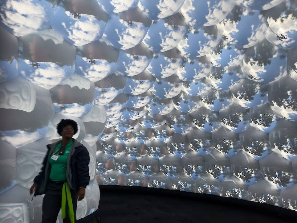 the interior of an architectural, inflatable compound camera installation with a person standing inside it, looking up at bubble-like forms featuring images of outside captured
