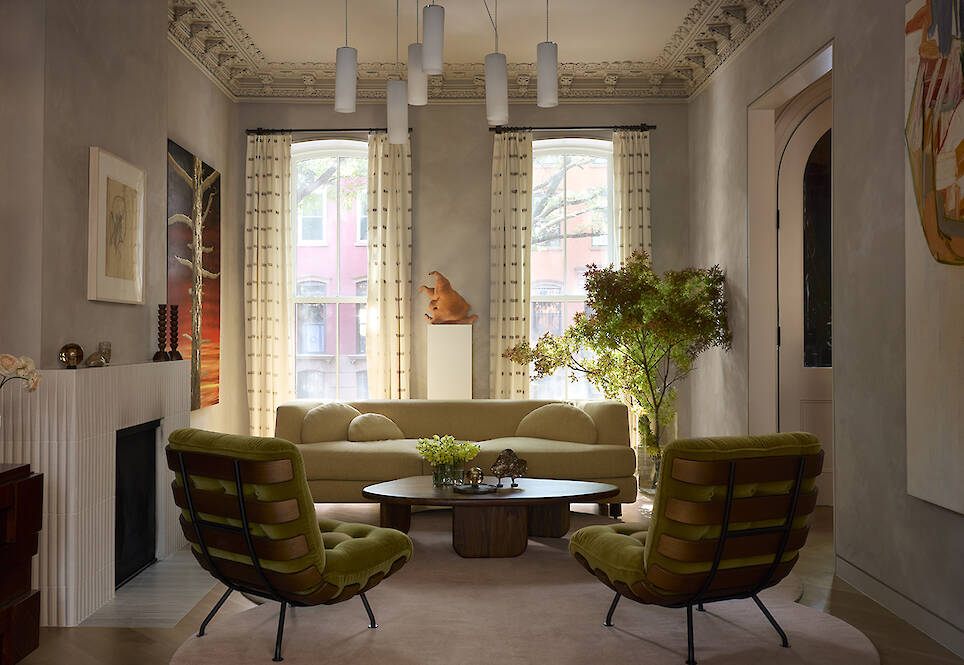 A living room with a beige sofa, two green lounge chairs, a wooden coffee table, and a fireplace with a decorative mantel