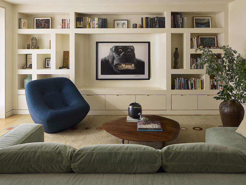 Living room with built-in bookshelves, a blue lounge chair, a wooden coffee table, and a framed gorilla print on the wall