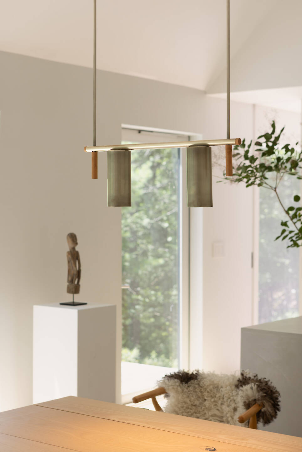 A minimalist pendant light with two cylindrical shades suspended over a wooden table