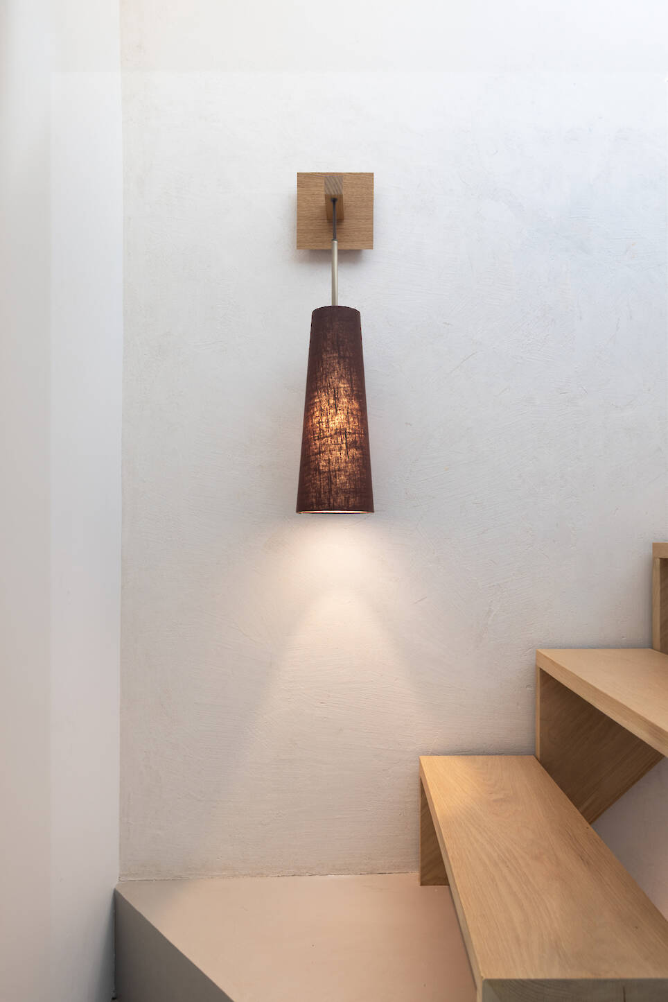 A conical pendant wall lamp with a dark fabric shade mounted above wooden stairs