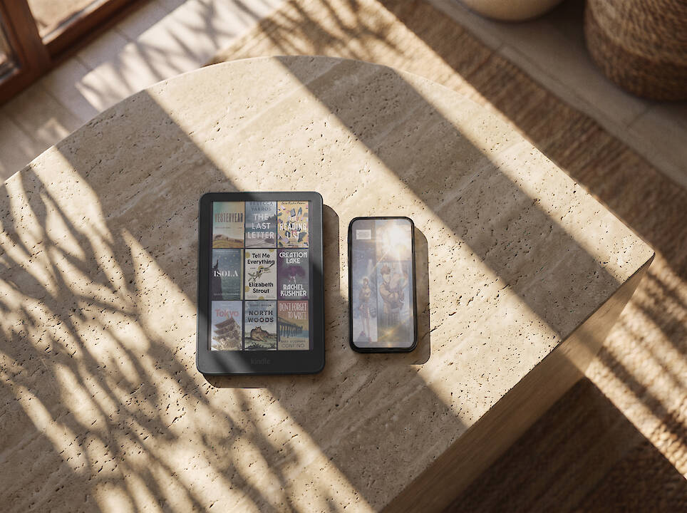 A Kindle redesign featuring a library of book covers on an e-reader next to a smartphone on a stone table