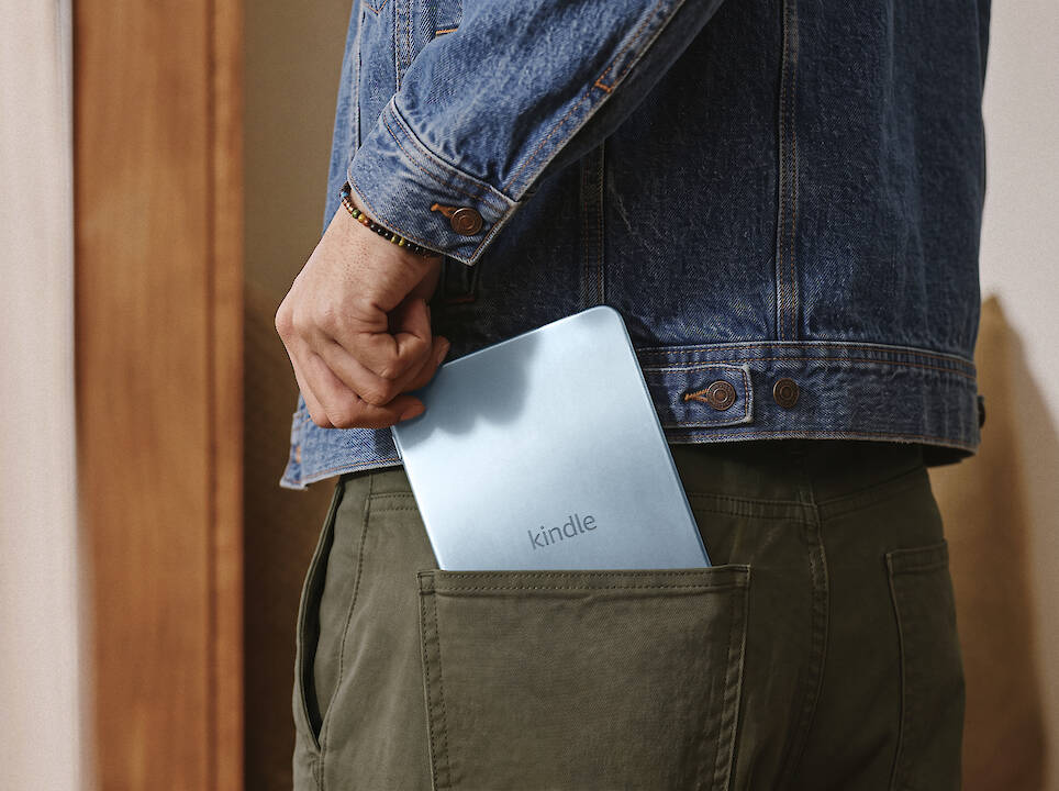 A person in a denim jacket tucking a light blue Kindle redesign into their back pocket