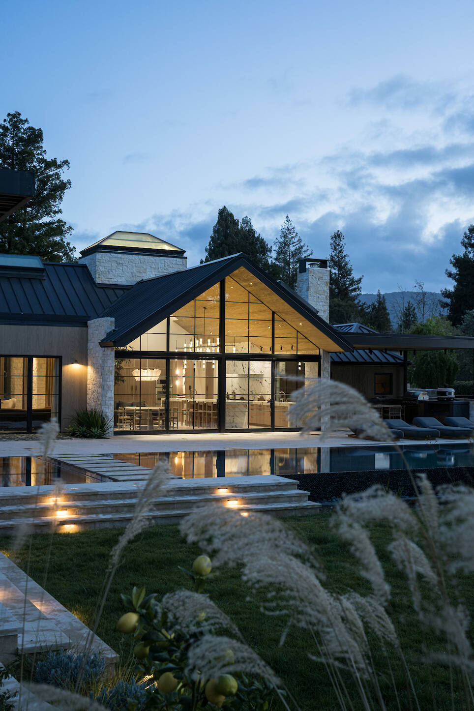 Modern house with large glass windows overlooking a swimming pool at dusk