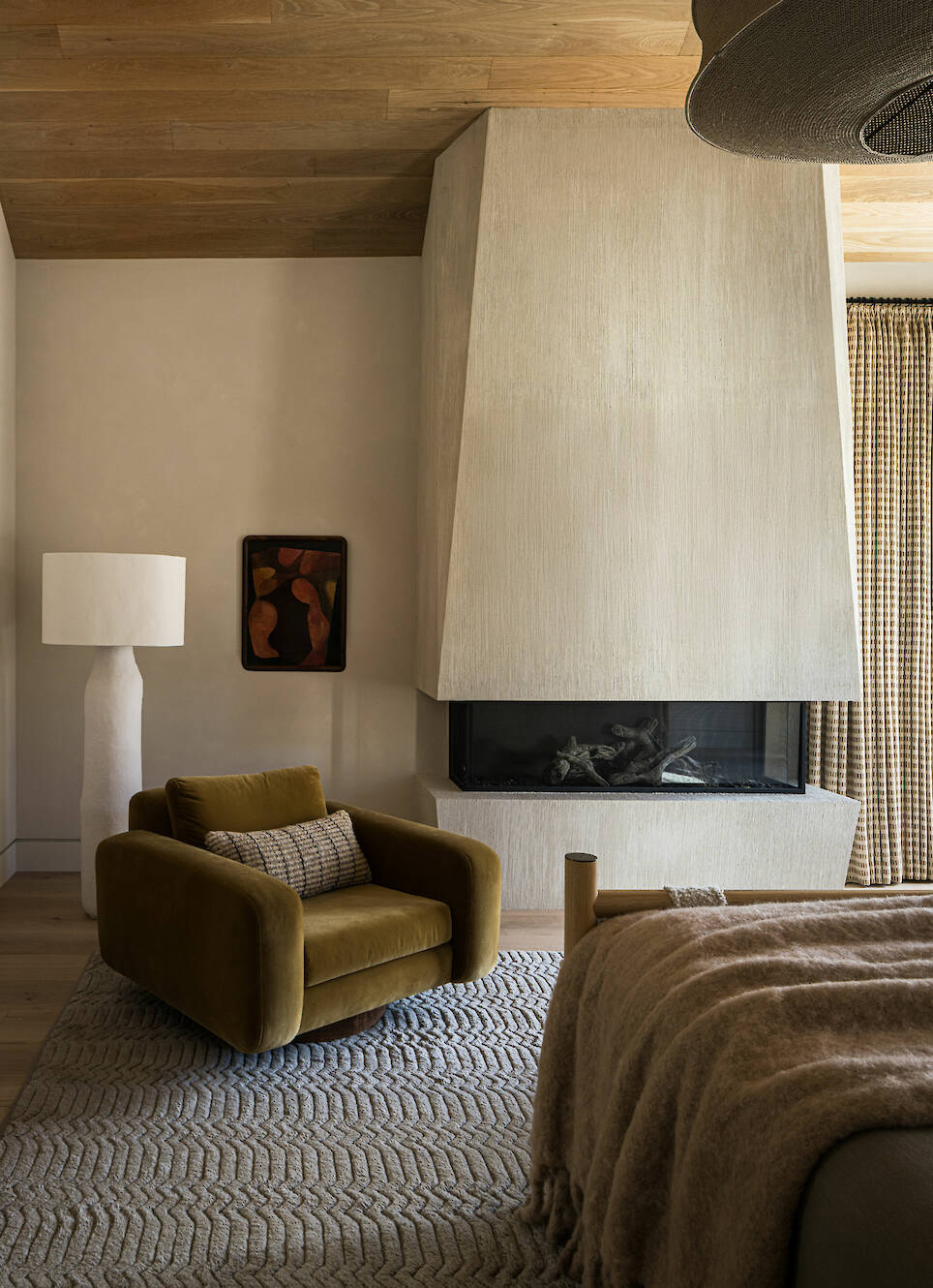 A modern room with a large textured fireplace, an olive green armchair, and a bed